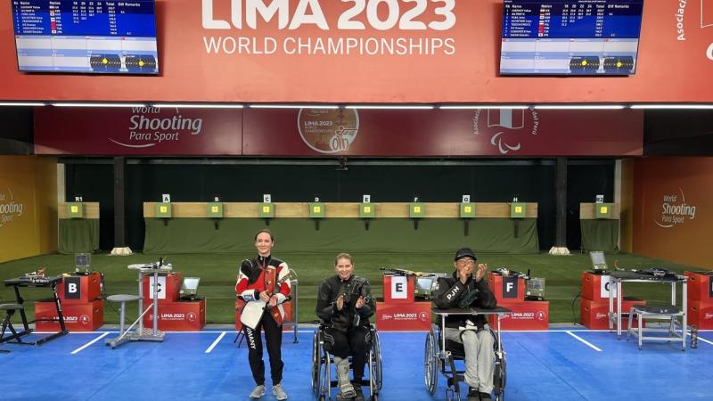 A standing woman next to a woman and a man in wheelchairs in a shooting range