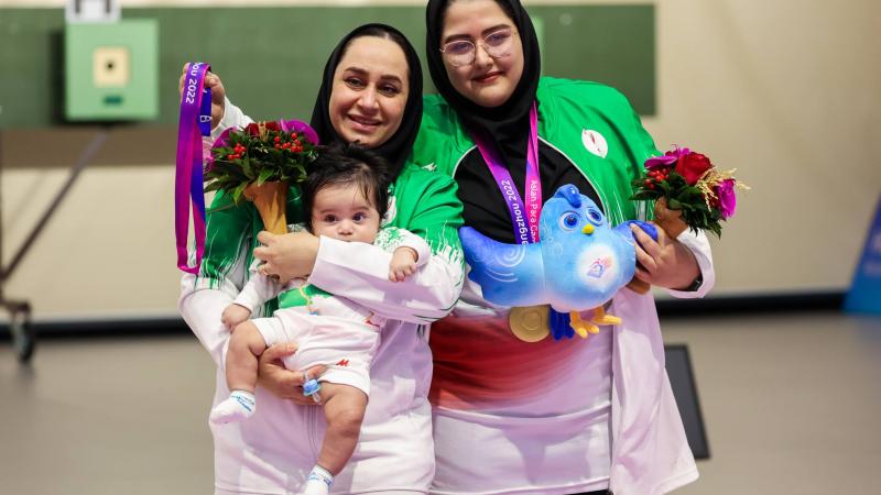 A woman with a headscarf holding a baby next to another woman with a headscarf in a shooting range