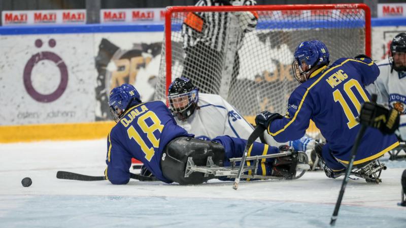 Two Swedish players in front of the Finnish goaltender in a Para ice hockey game