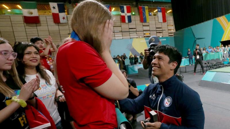 A man in a wheelchair proposing to a standing woman in a competition arena