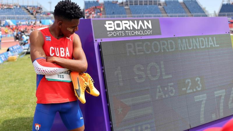 A man standing next to a screen showing his world record on an athletics field