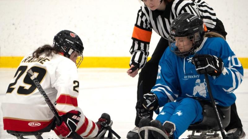 A Para ice hockey official throwing a puck between two female players