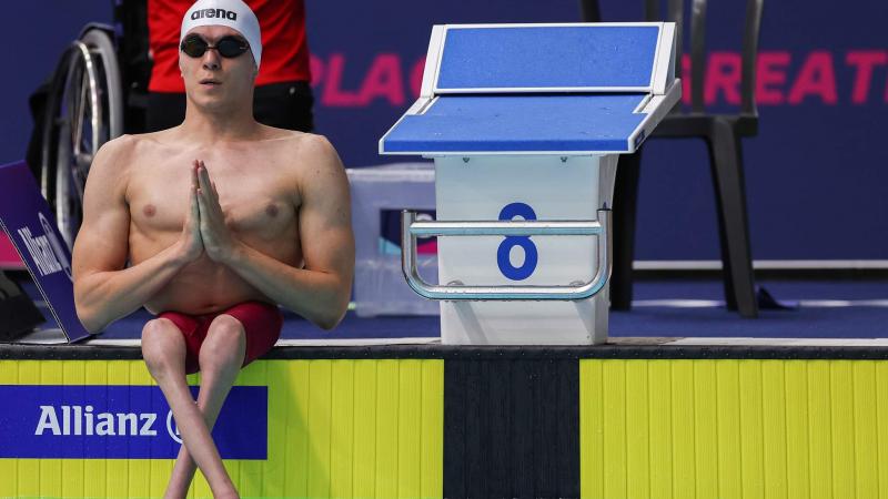 A male Para swimmer seated next to a starting block by a swimming pool