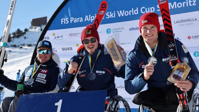 Three male sit skiers pose for a photo on the podium.