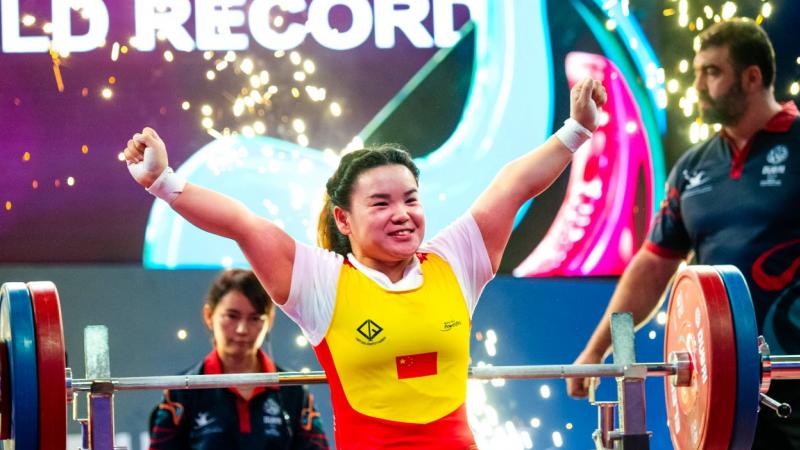 A female athlete on a bench press celebrating with two people in the background