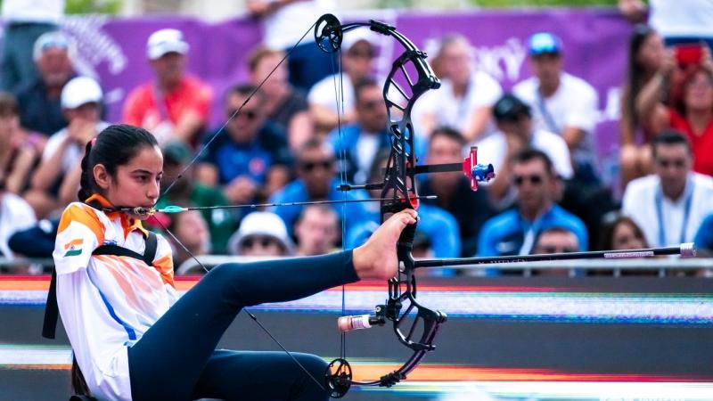 A female athlete without arms aims her shot by holding the bow with her right leg.