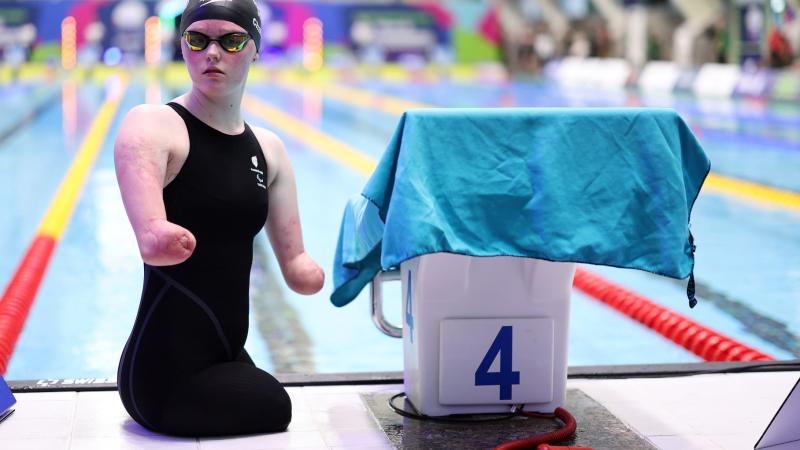 A female Para swimmer next to the starting block of a swimming pool