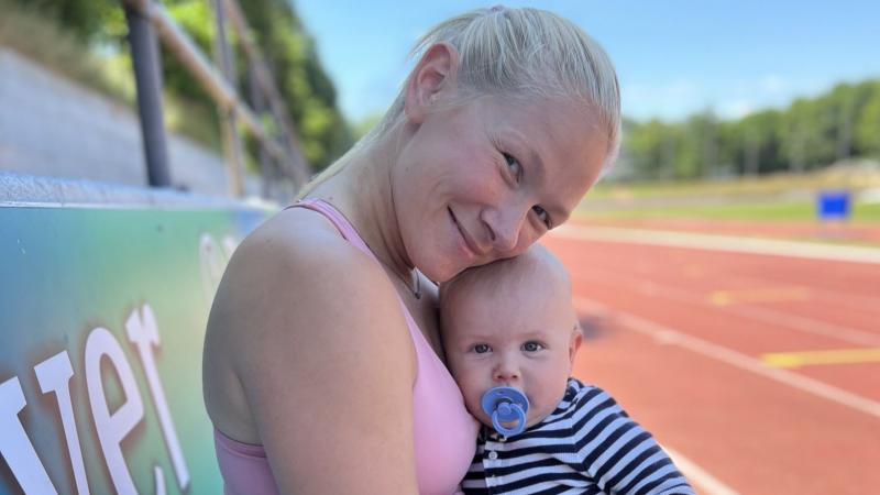 A female athlete sits by the tracks and holds a baby boy.