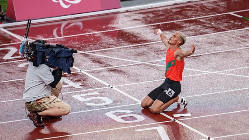 A male athlete celebrates in front of a camera operator on the track after winning a race.