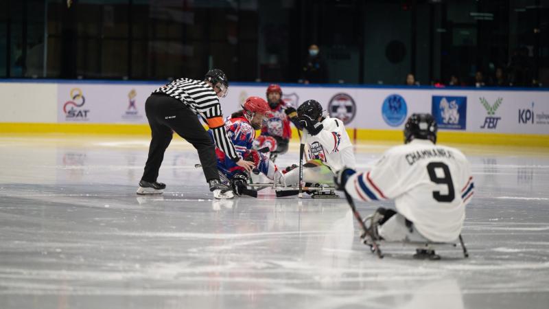 A Para ice hockey referee and two players on a face-off 
