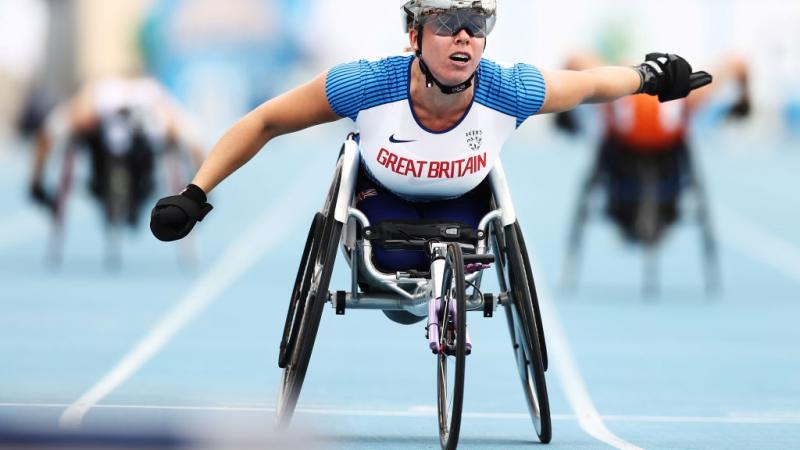 A female wheelchair racer crossing the finish line ahead of two competitors