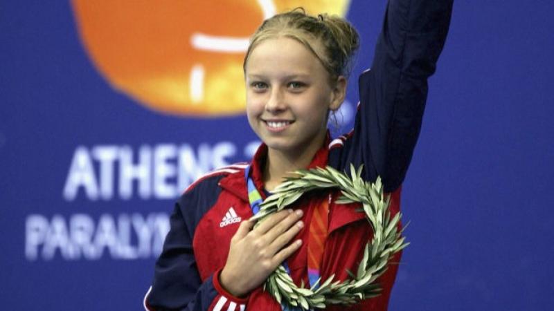 A young female athlete waves her left hand after receiving a gold medal.
