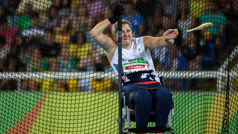 Kylie Grimes seated throws a wooden club 