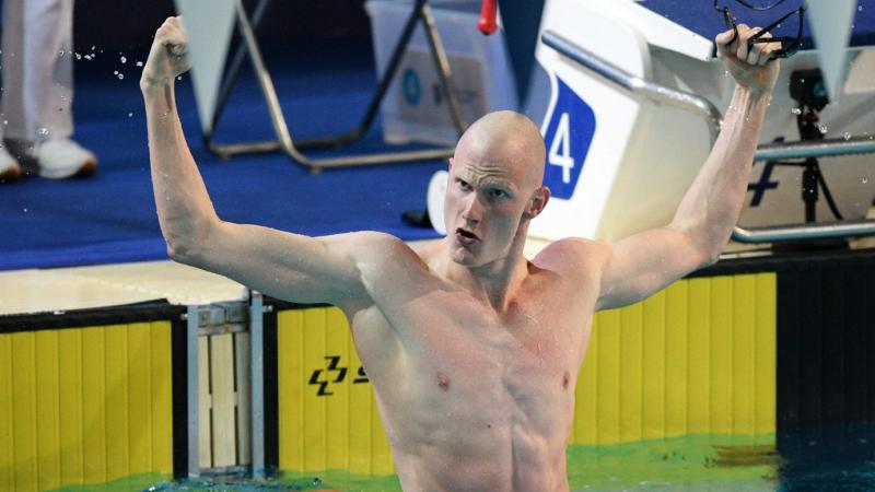 A male swimmer open his arms to celebrate in the pool