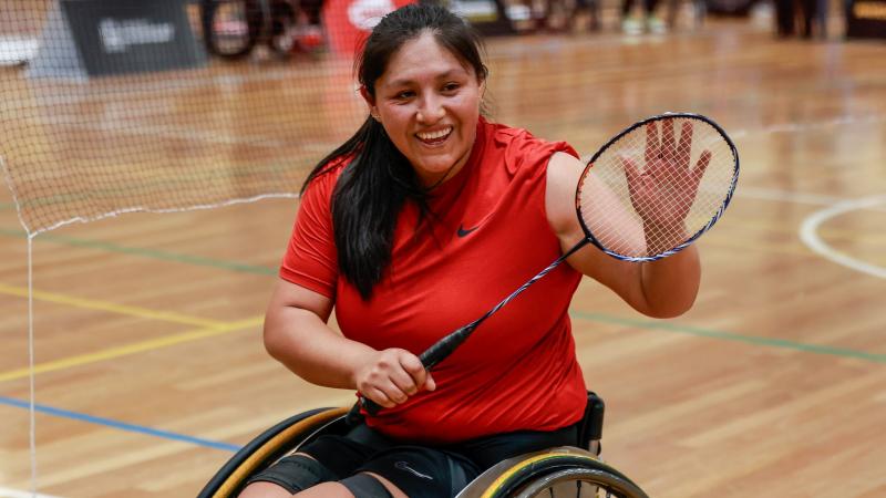 A female Para badminton player, who competes in a wheelchair, holds a racquet and smiles