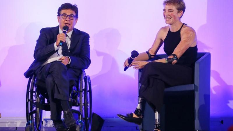 A male official and a female Paralympic athlete are speaking during a conference.