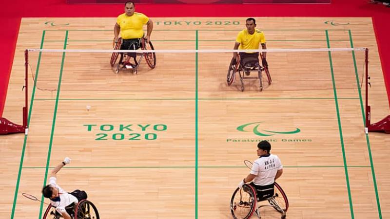Two teams of wheelchair badminton players wait for serve on court