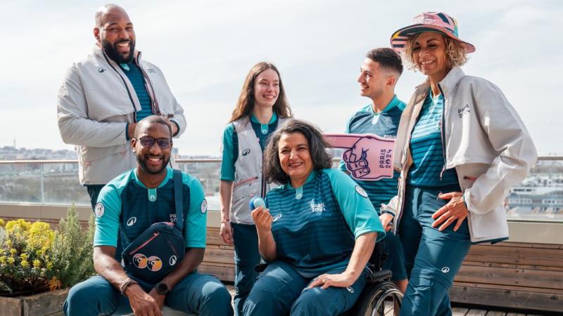 Six male and female volunteers pose for a photograph wearing the Paris 2024 volunteer uniform.