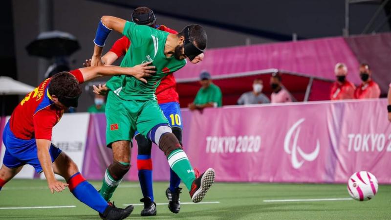 A male blind football player wearing a green uniform runs past two players