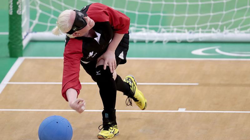 A female athlete throws a blue ball in front of the net during a goalball game. 