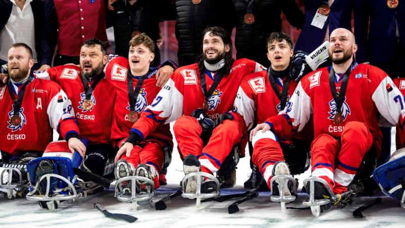 A group of Para ice hockey players with a group of standing people behind them