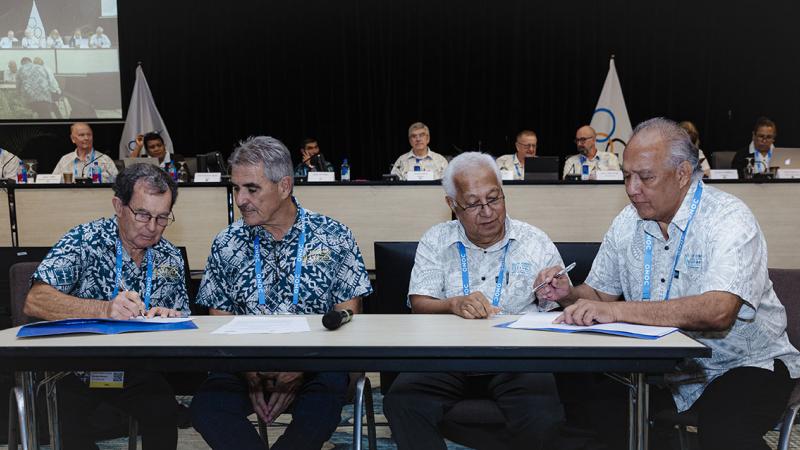 Four male officials sign a document