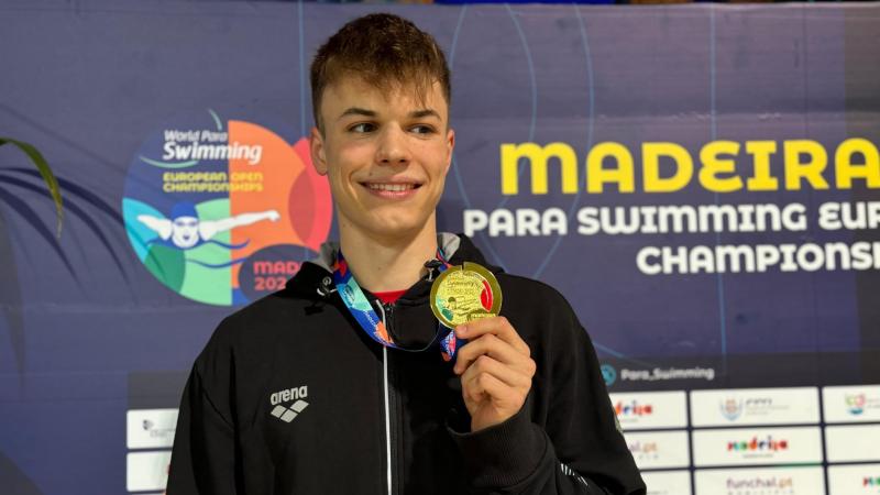 A man showing his gold medal on a podium