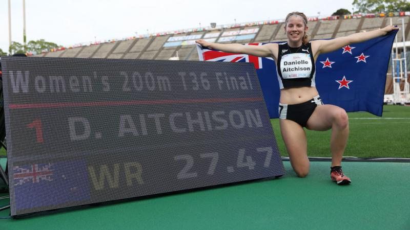 A young female athlete posing for a picture next to a screen showing a world record