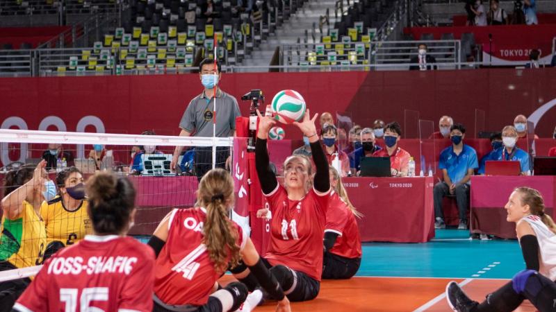 A female sitting volleyball athlete sets the ball during competition