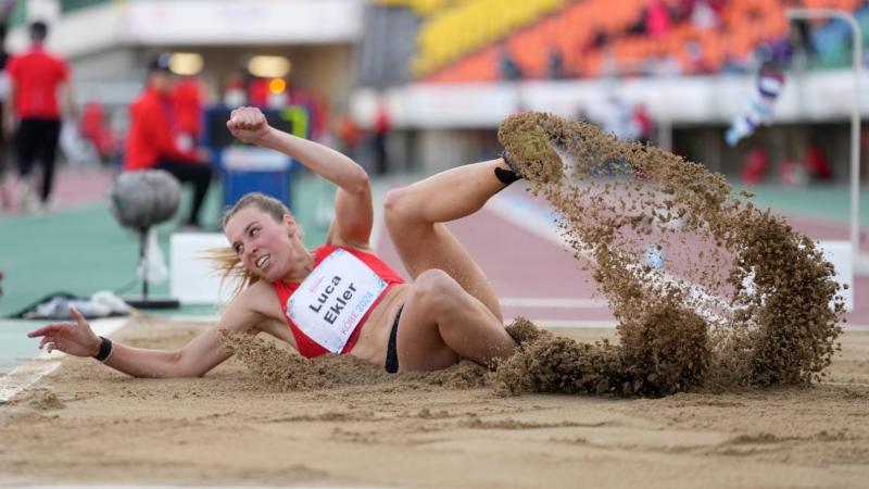 A female athlete landing in the sand in a long jump event