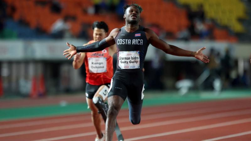 A male athlete with prosthetic leg crossing the finish line ahead of another competitor