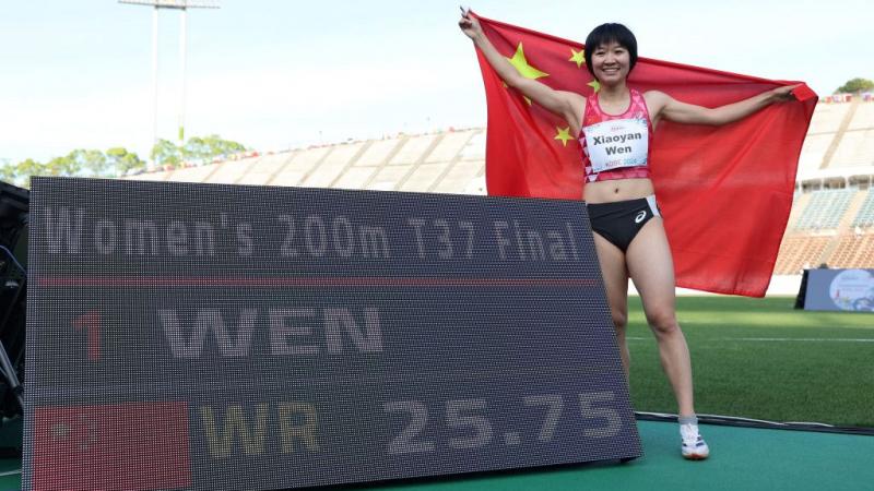 An athlete with the Chinese flag posing next to a scoreboard