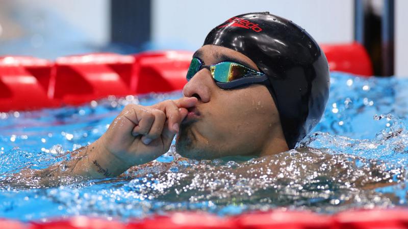 A male Para swimmer holds his hands to his lips in the pool after a competition