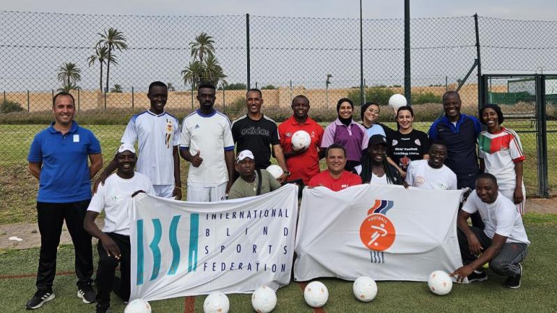 Sixteen people pose for a photograph with IBSA flags