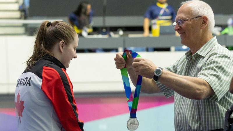 A man giving a silver medal to a female swimmer 