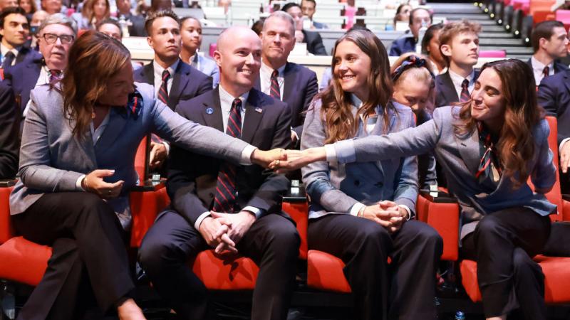 Four people sit side by side, with two of them holding each other's hands to celebrate