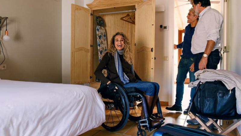 A female wheelchair user enters a bedroom and smiles