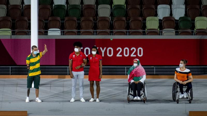 Four athletes and a guide wearing face masks are being presented. 