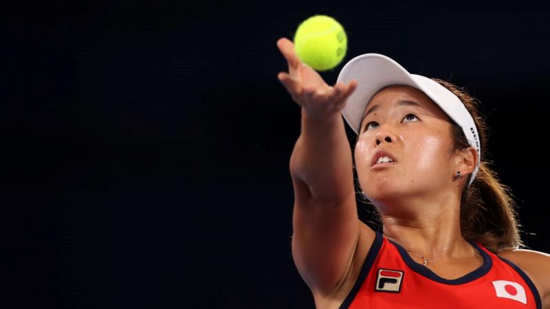 A female wheelchair tennis athlete throws the ball before a serve