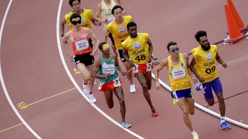 A runner and his guide ahead of three other runners with guides in a race