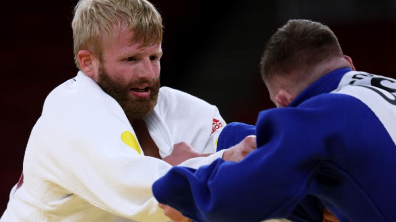Two male judo athletes are grappling, grabbing their judogis during competition