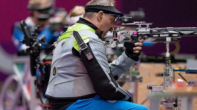 A male athlete competing in a shooting Para sport range in front of other athletes