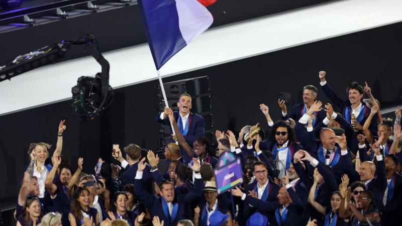French athletes taking part in the Paris 2024 Parade of Nations. A male athlete is waving the French flag.