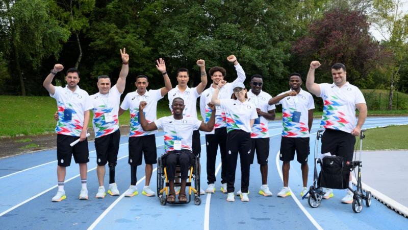 Ten people - eight athletes and two guide runners - pose for a photo on a track. They are wearing watching uniforms