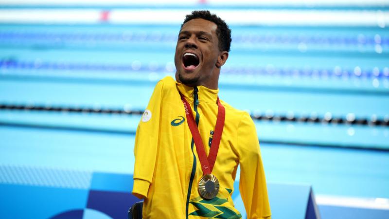A man in a yellow jacket wears a gold medal and happily yells