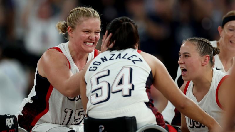 Two female wheelchair basketballers hug in celebration on the court