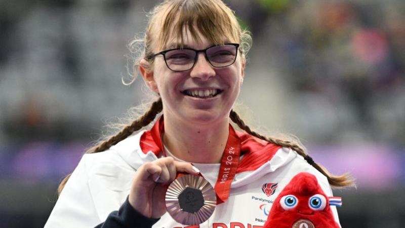Para athlete Anna Nicholson holds up a bronze medal and smiles 