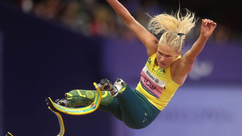 A woman with prosthetic legs is mid-air during a long jump competition