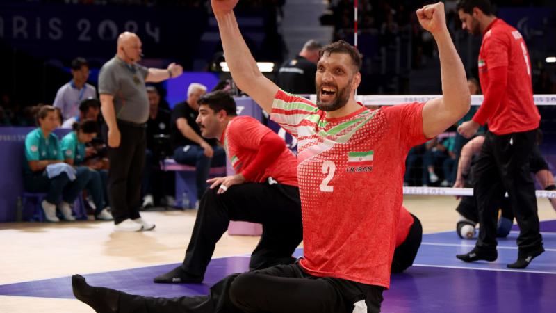 A sitting volleyball player raises his arms in celebration while on the volleyball court