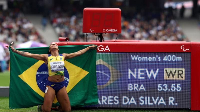 A Brazilian female athlete kneeling next to a screen with her world record